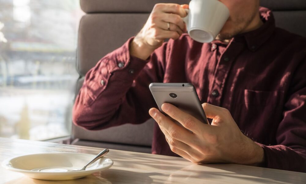 Uomo beve un caffè seduto al bar guardando lo smartphone