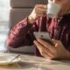 Uomo beve un caffè seduto al bar guardando lo smartphone