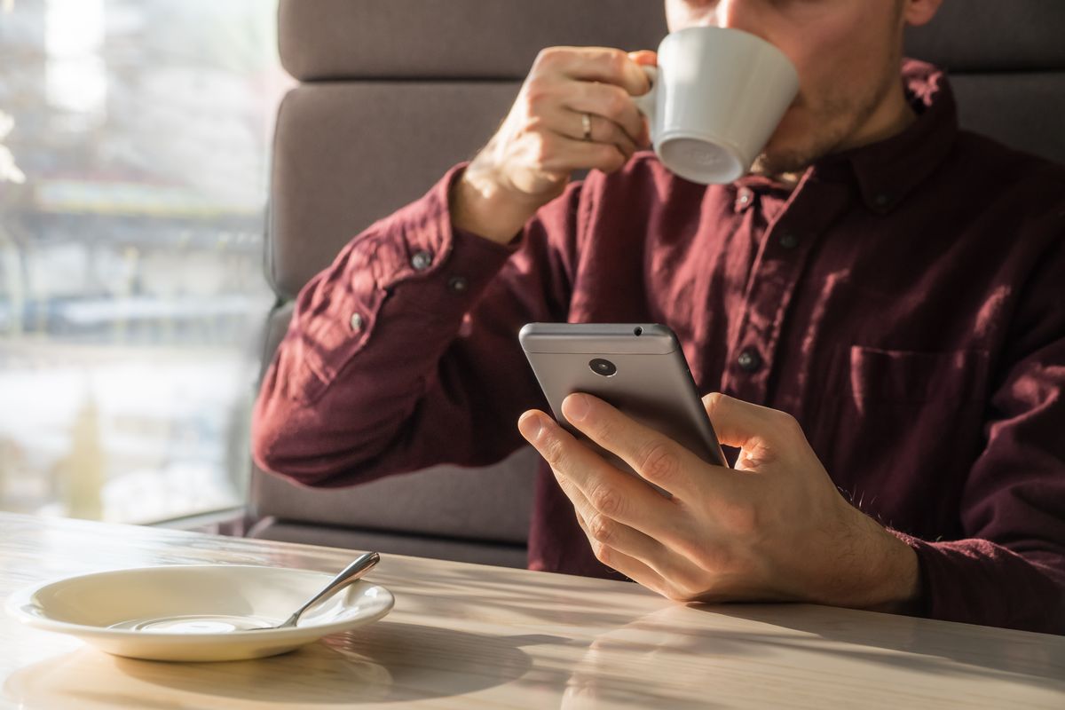 Uomo beve un caffè seduto al bar guardando lo smartphone