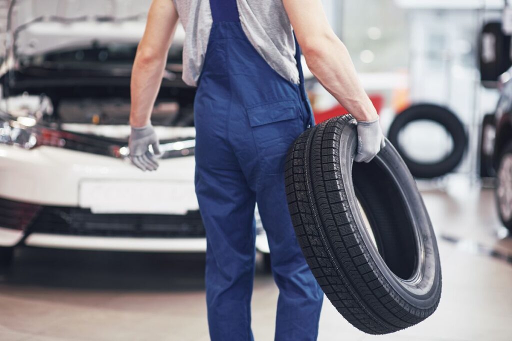 Meccanico che porta una gomma per cambiarla ad un'auto