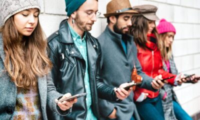 Gruppo di persone appoggiate al muro che guardano il proprio smartphone