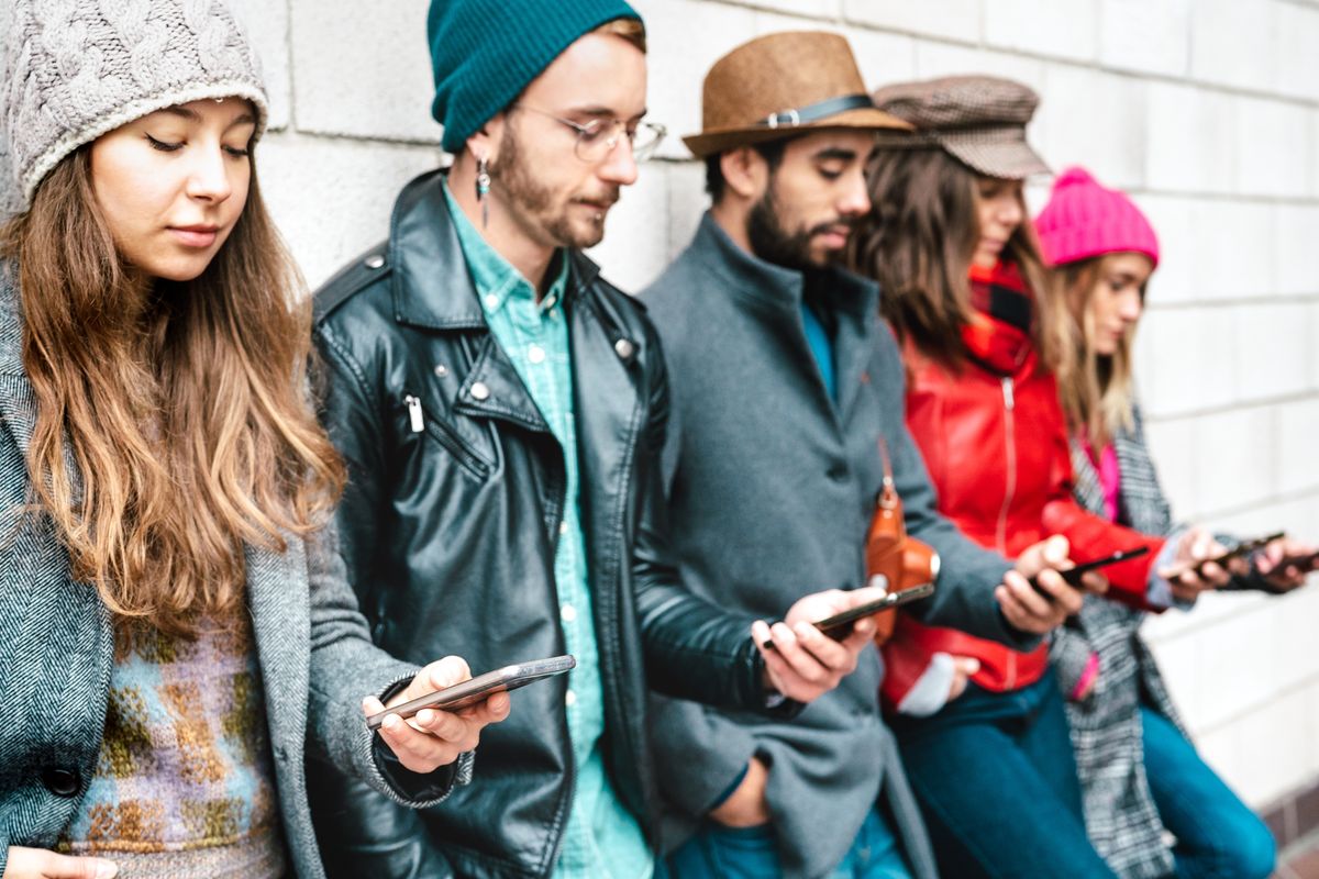 Gruppo di persone appoggiate al muro che guardano il proprio smartphone