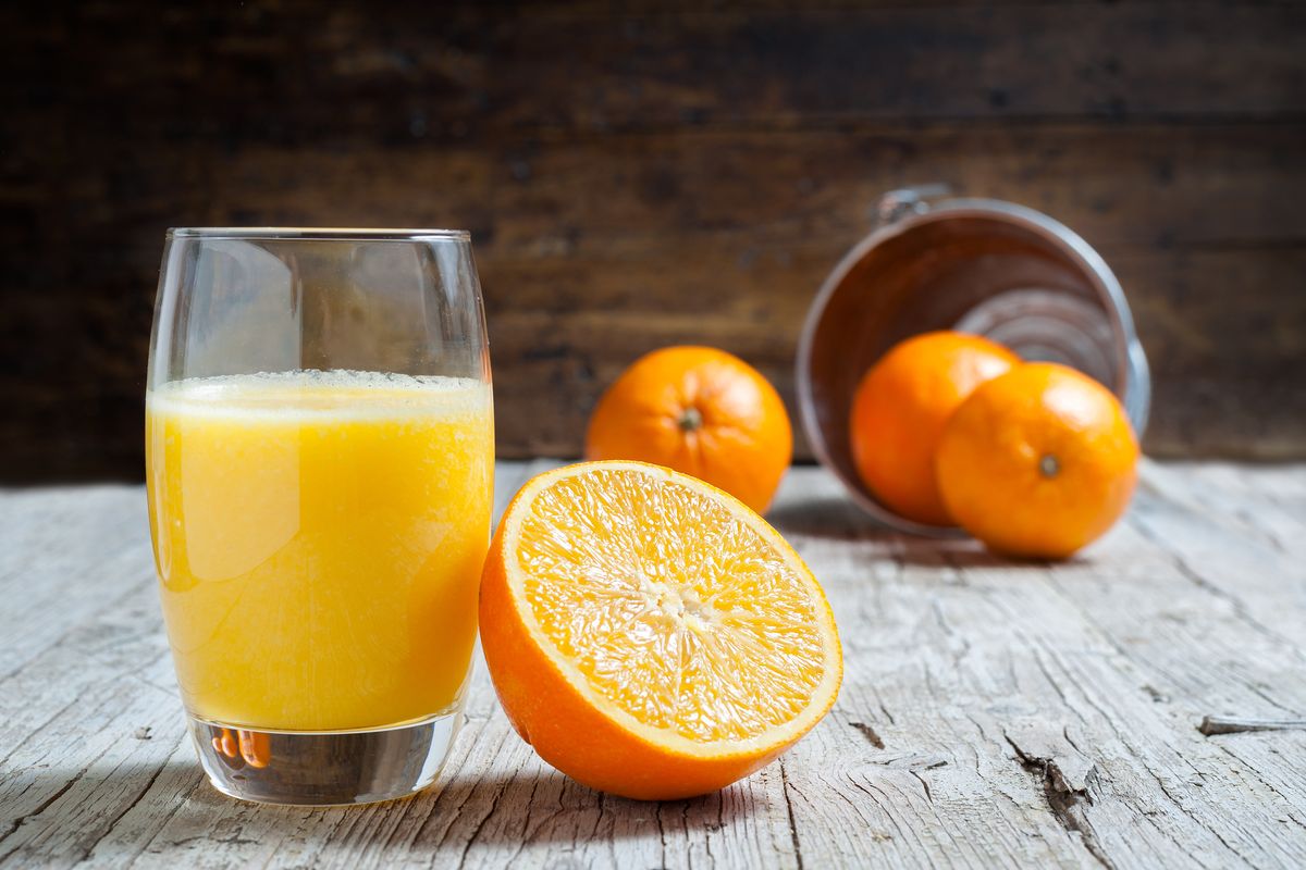 Bicchiere di succo d'arancia con degli aranci sul tavolo