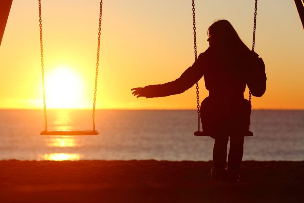 Ragazza single che si dondola su una altalena al tramonto